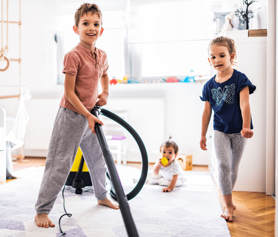 Boy vacuuming while younger sister and baby watch him