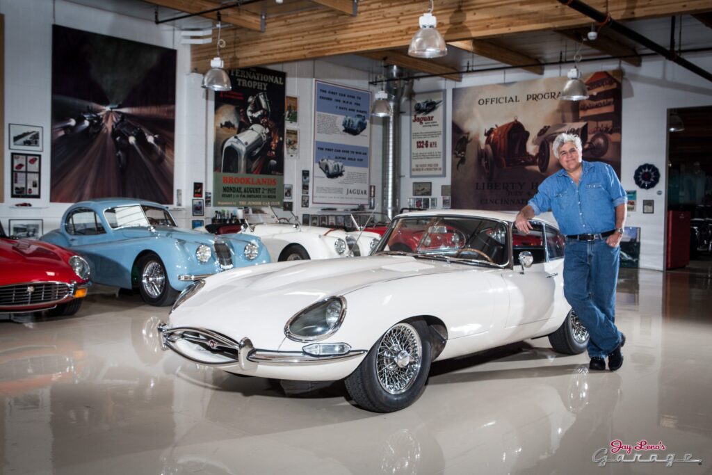 Jay Leno leaning against a car in his garage