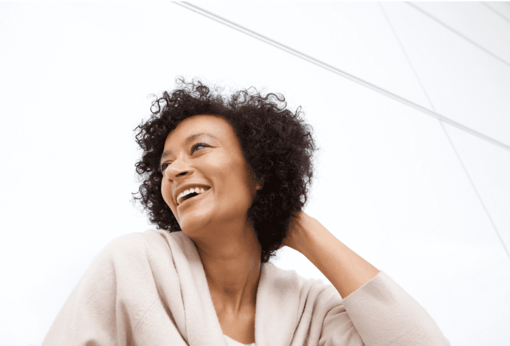 A smiling black woman in a white sweater against a white background looking joyful and at peace