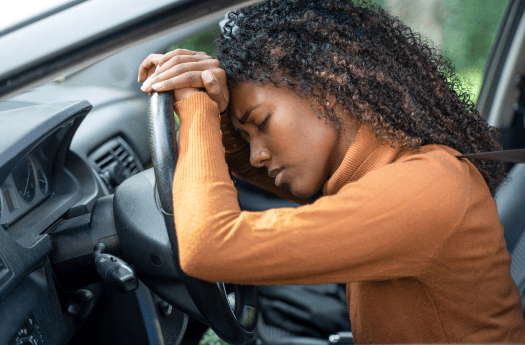 Overwhelmed woman with head and body bent over car's steering wheel
