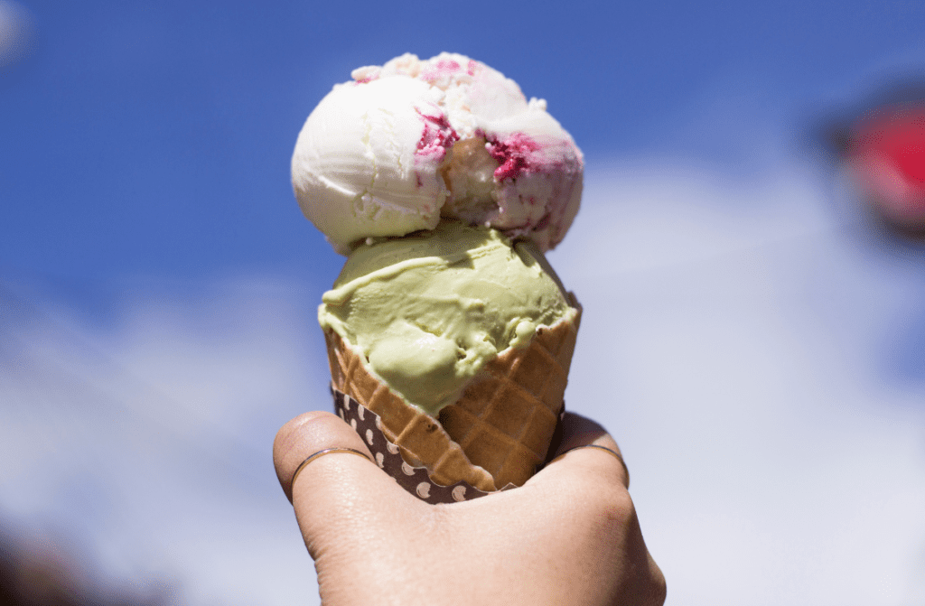 Child's hand holding a double scoop ice cream cone up to the sky.