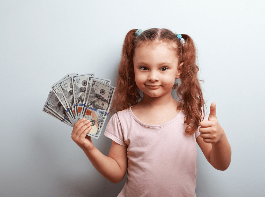 Cute little girl holding a bunch of dollar bills in one hand and showing a thumbs-up in the other hand.