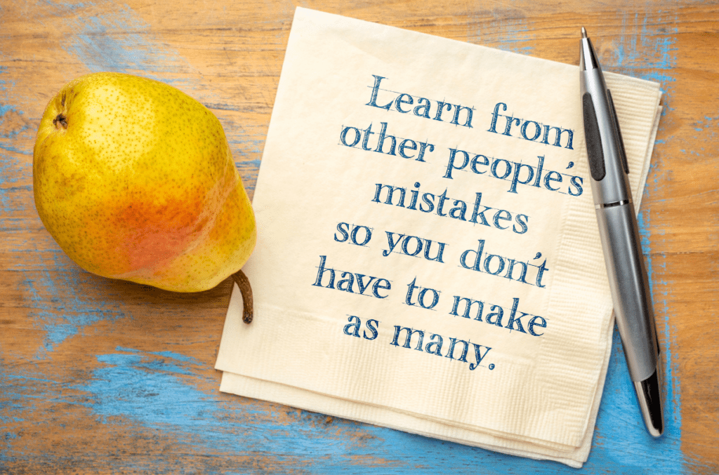 A pear is sitting on a table next to a note that says 'Learn from other people's mistakes so you don't have to make as many.'