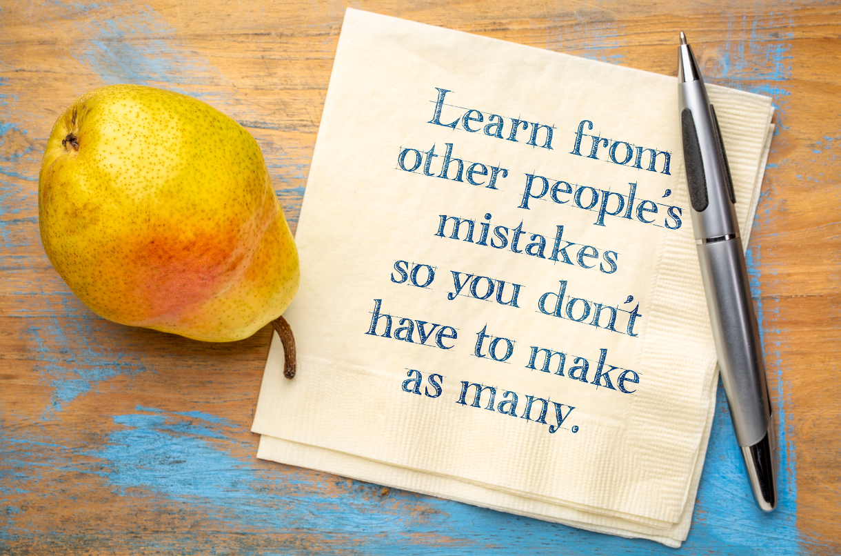 A pear is sitting on a table next to a note that says 'Learn from other people's mistakes so you don't have to make as many.'