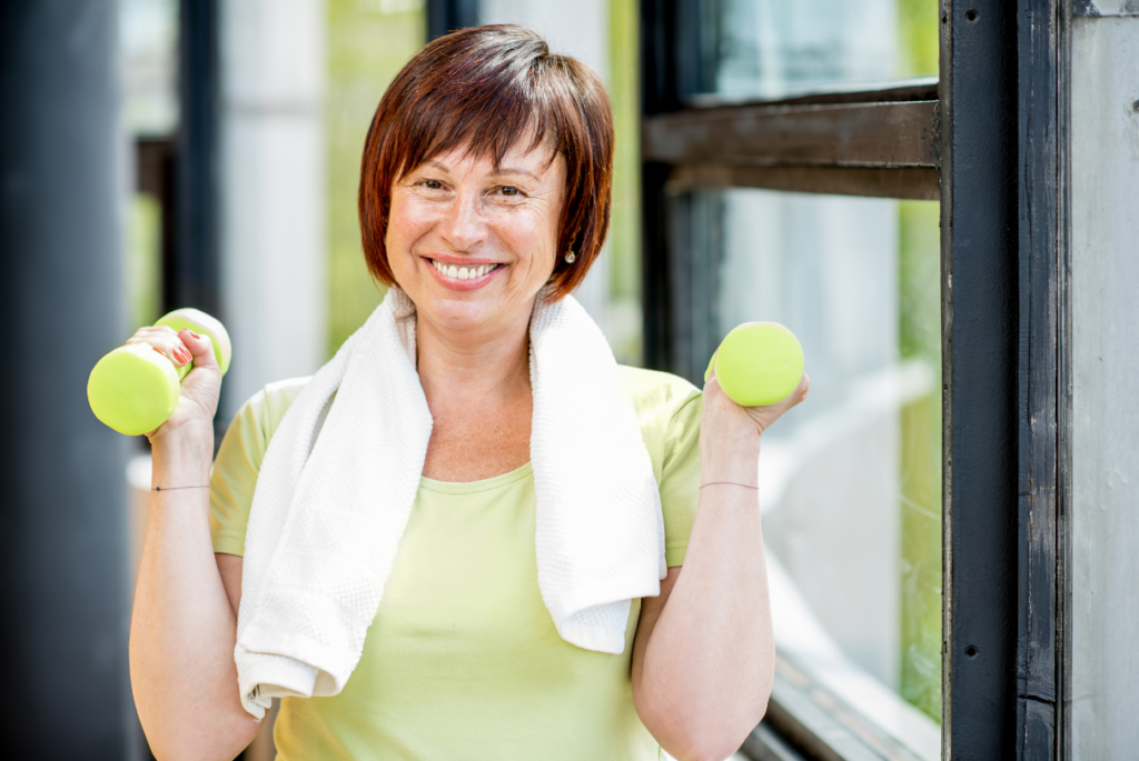 Smiling woman in a lime green tshirt holding lime green dumbells with a sweat towel around her neck