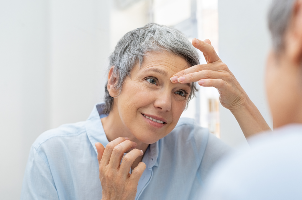 Smiling 60-year-old woman looking at her gray hair and wrinkles in a mirror