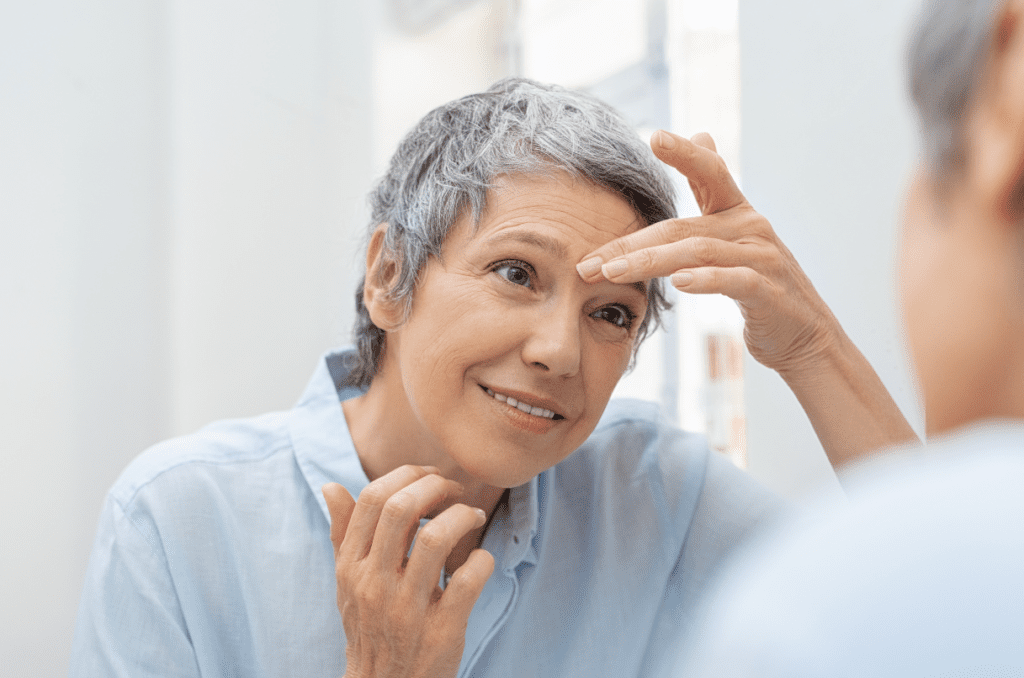 Smiling 60-year-old woman looking at her gray hair and wrinkles in a mirror