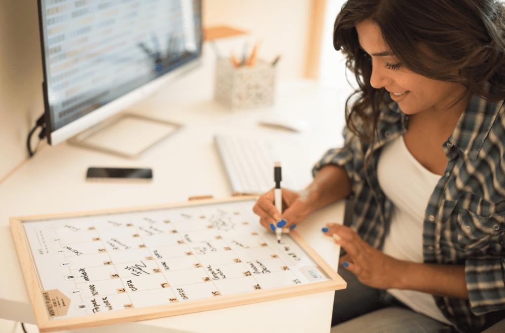 Smiling young woman marking dates on a calendar white board.