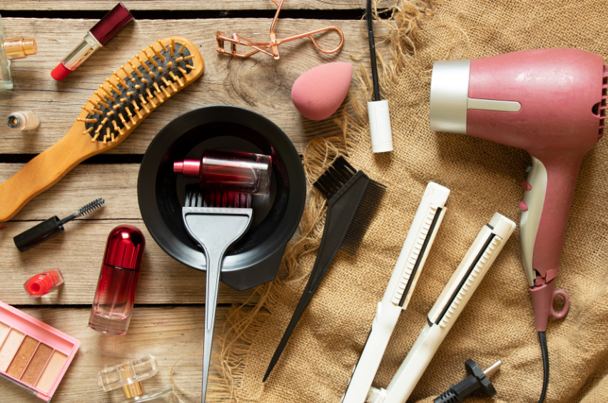 The inside of a bathroom drawer with make=up, hairdryer, hair straightener, and other beauty aids