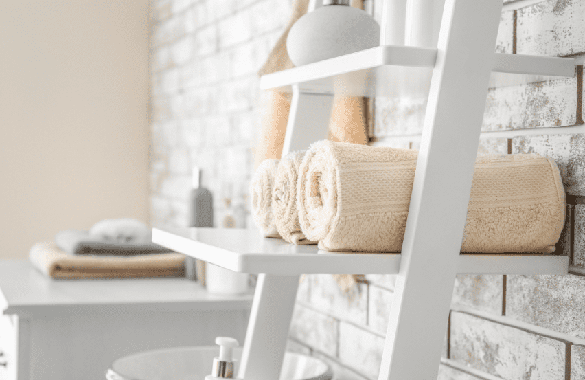 A ladder rack in a bathroom holding linens and other bathroom items