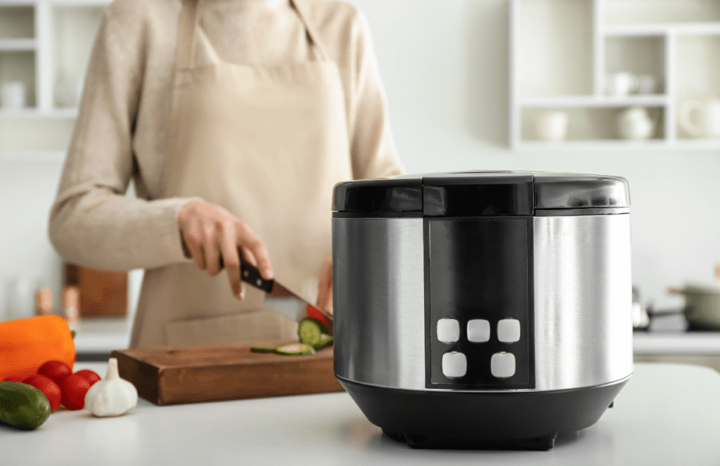 Woman in the background slicing food on a cutting board to put in crock pot which is in the foreground