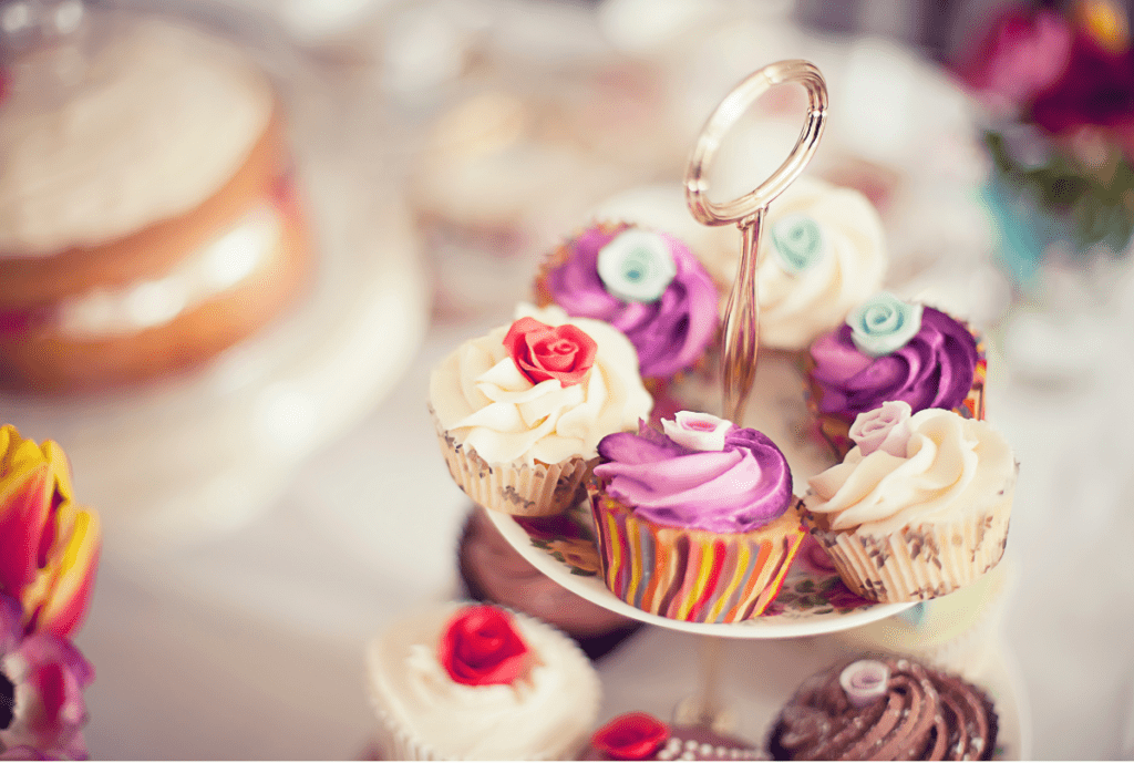 A tiered-plate of colorful cupcakes is in the foreground and blurred cakes are in the background