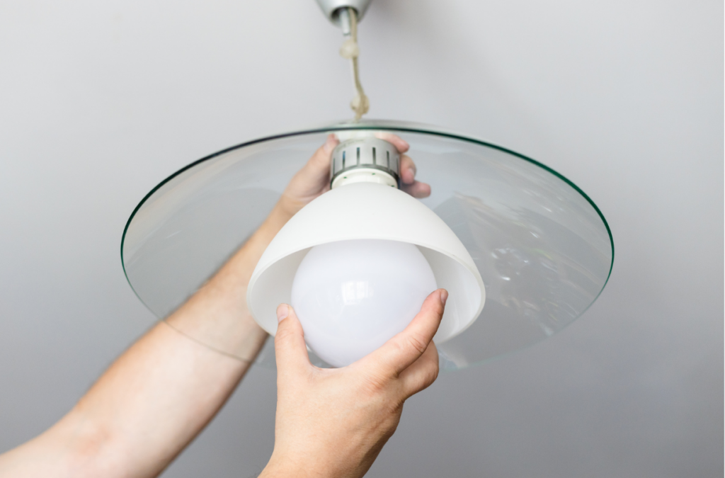 Hands screwing a lightbulb into a kitchen light fixture