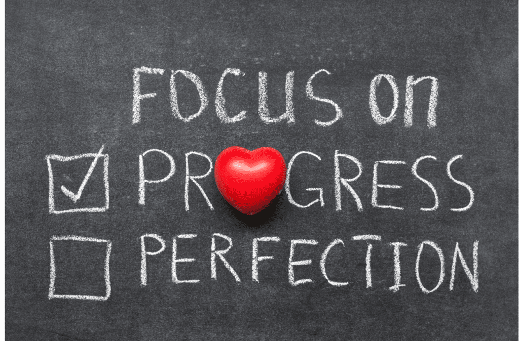 Blackboard with chalk writing that that says "Focus on" and then has two check-off boxes saying "progress" and "perfection"