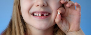 Head shot of a little girl holding her tooth that just came out