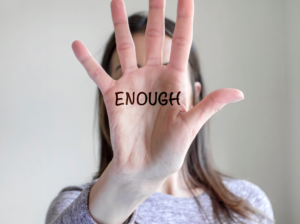 Woman holding a hand in front of her face with the word 'enough' written on her hand in marker