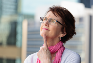 Mature woman looking up into the sky with her finger to her chin as if she's pondering something