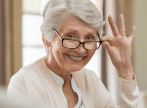 Head shot of a mature, smiling woman who is tipping her glasses down a little bit.